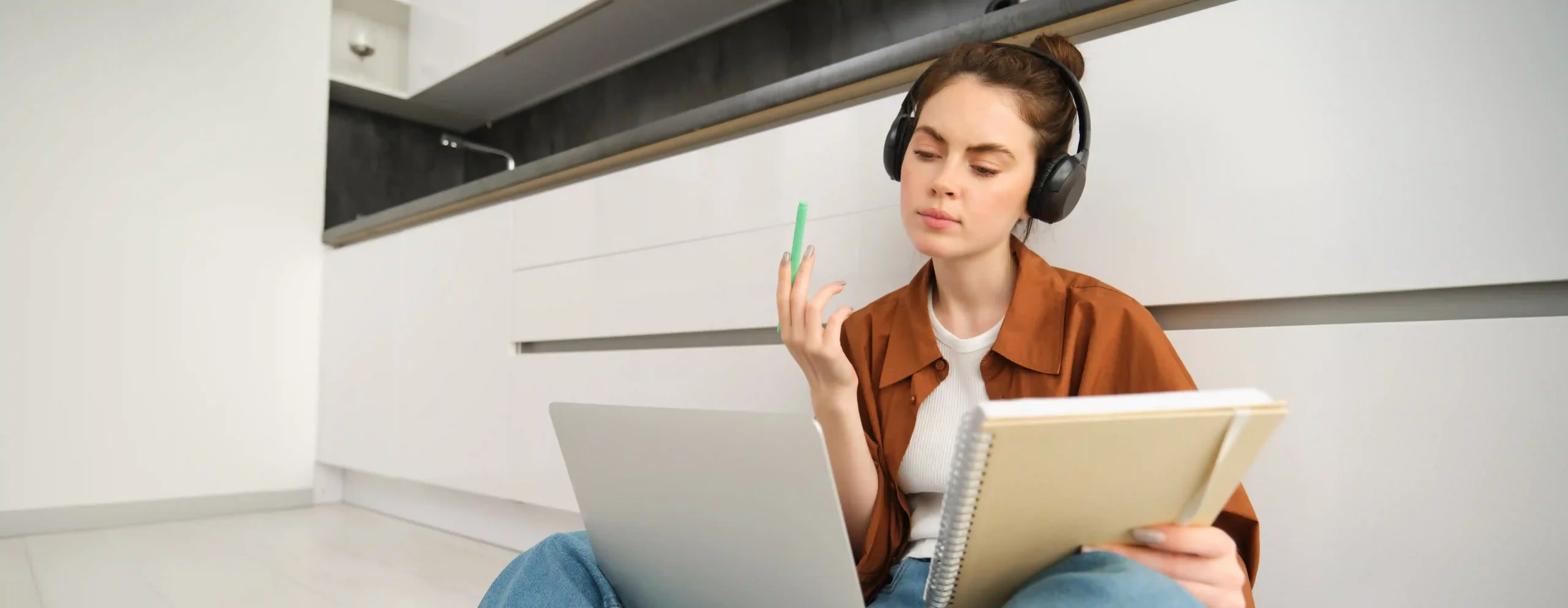 Young woman studying remotely at home with headphones, a laptop, and a notebook, highlighting the benefits of distance education like flexibility and convenience.